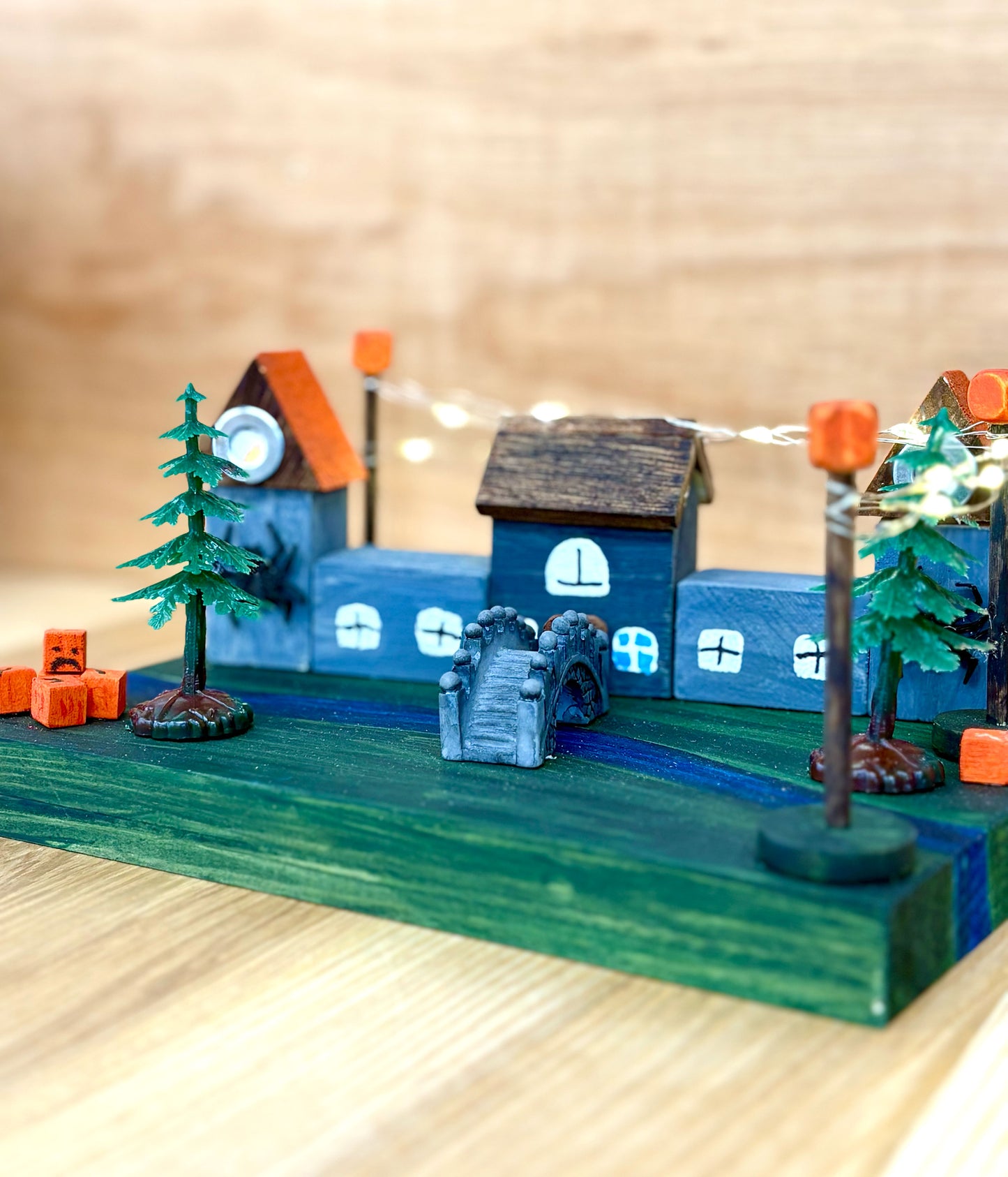 Model castle scene with houses, trees, and lights on a wooden base.