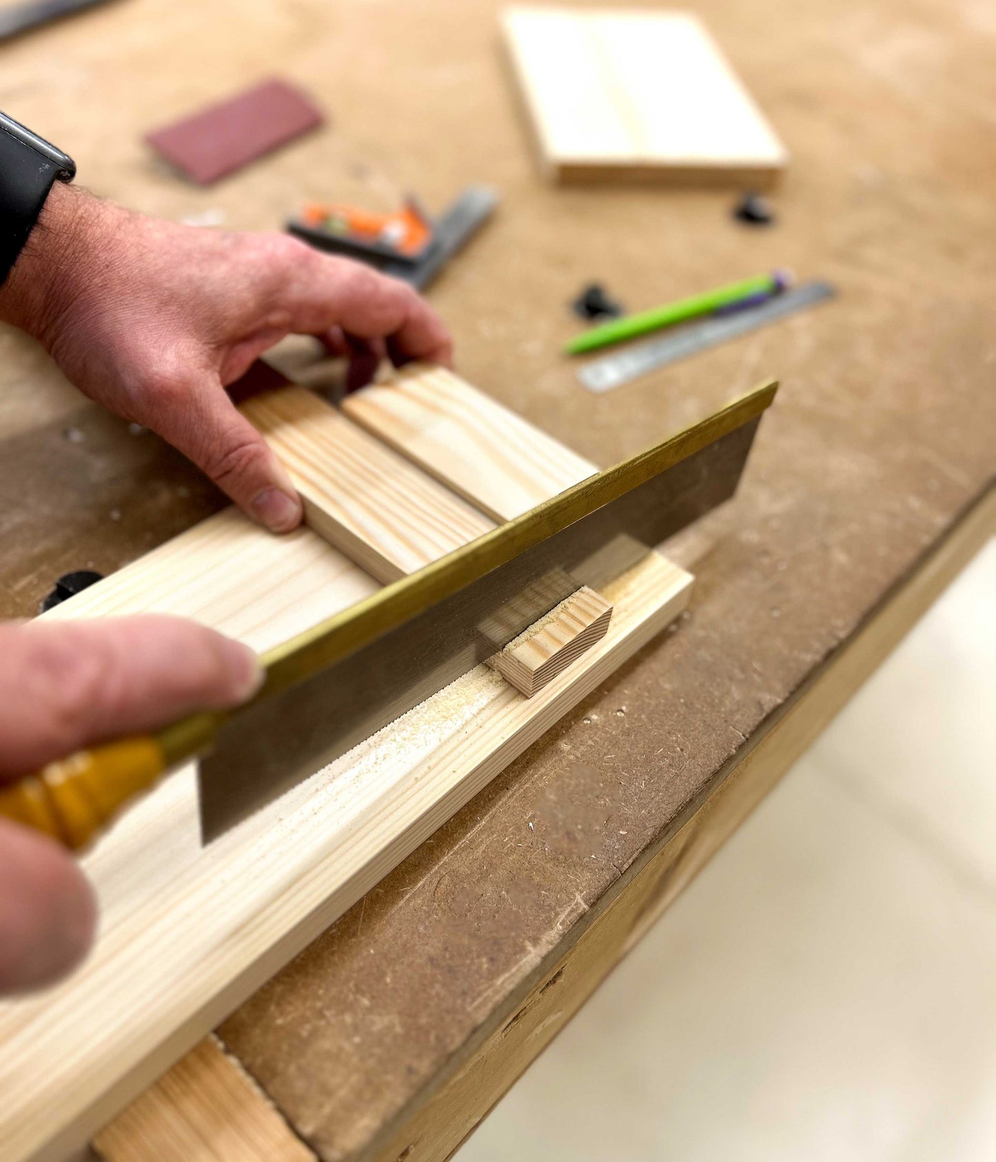 Using a fine woodwork saw to learn how to cut straight and true on a workbench in Ash & Co Workshops