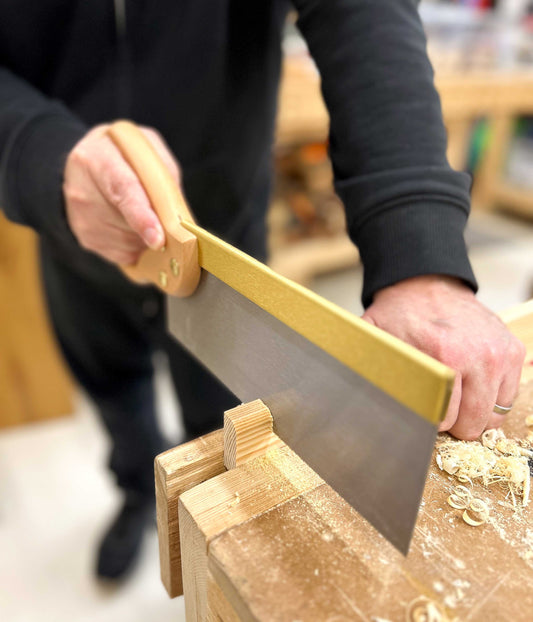 A beginner woodworker uses a fine woodwork saw to cut wood in a vice at a workbench in Ash & Co Workshops
