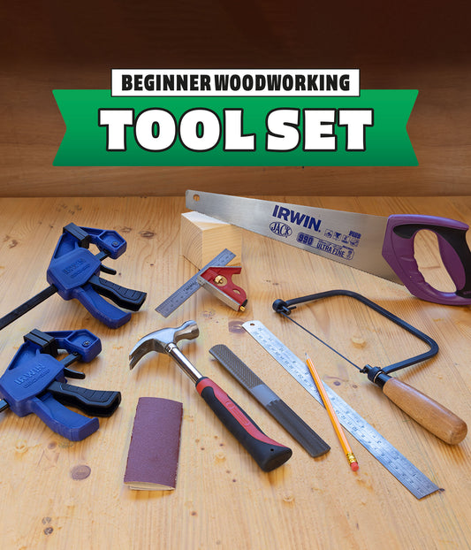 A beginner woodworking tool set arranged on a light wood surface, including blue clamps, an Irwin hand saw, a square, a hammer, a file, a pencil, a saw blade, and a sanding block, with a green banner reading 'BEGINNER WOODWORKING TOOL SET' above.