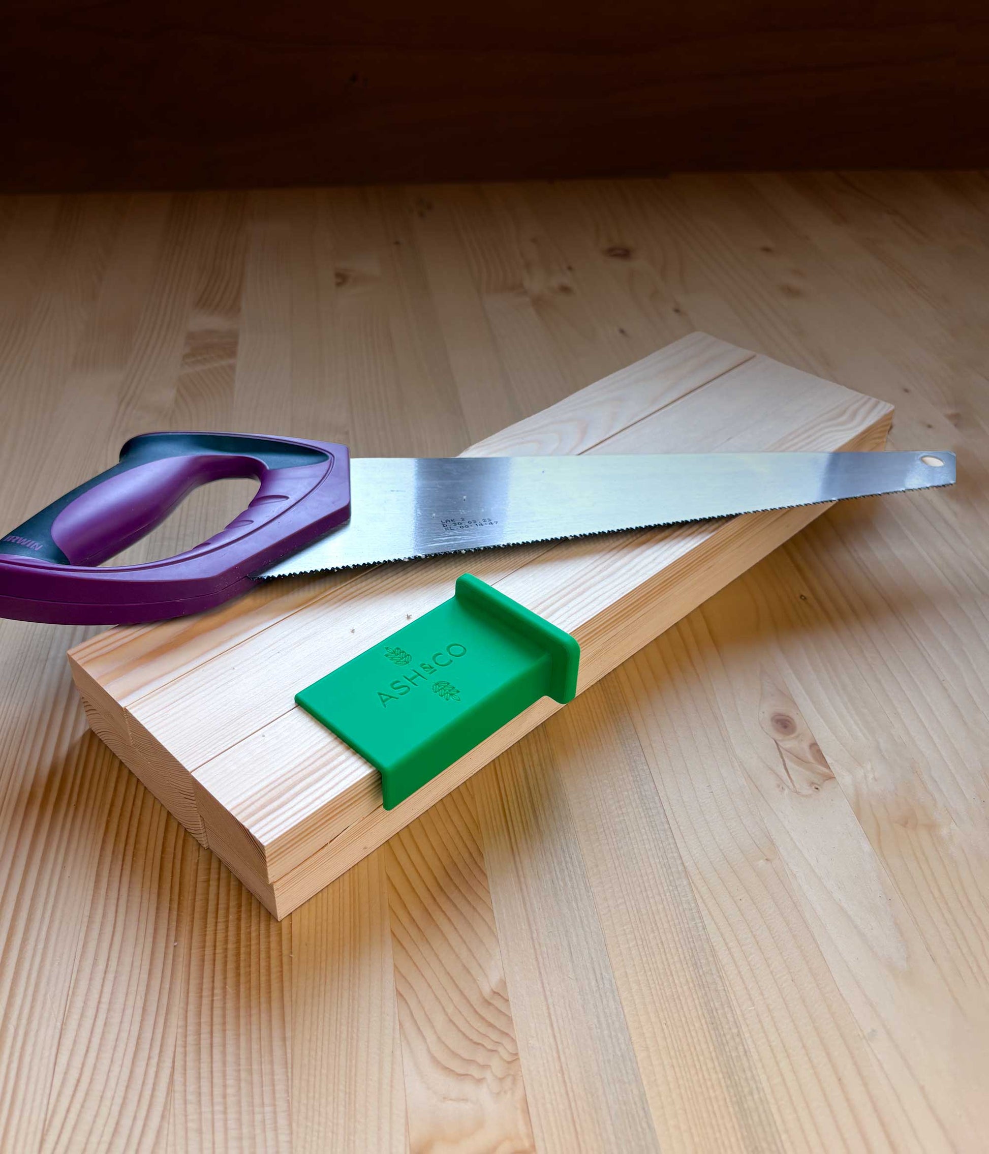 Wooden pine practice pieces with a fine-tooth saw and green 3D printed saw guide on a wooden surface