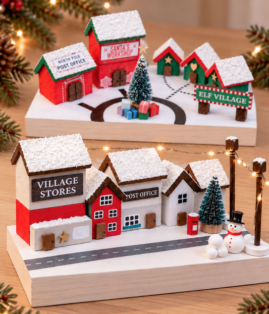 Two finished wooden Christmas village craft kits showing the Elf Village and Christmas Village miniature scenes side by side. Christmas-themed villages with miniature houses and decorations on a wooden base - Christmas craft kits for kids and families from Ash and Co Workshops.