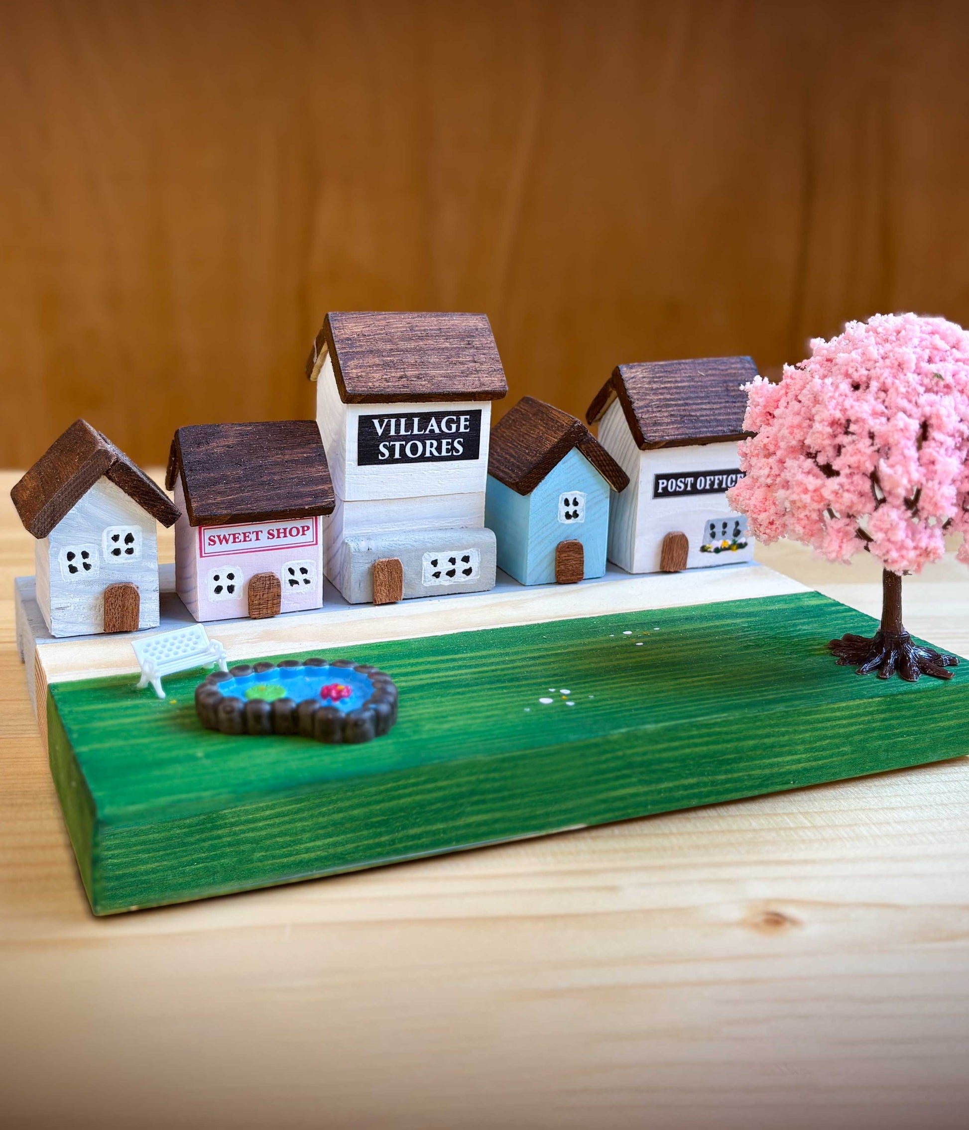 Wooden craft kits for kids - completed model village with miniature houses and a pink tree on a wooden base.