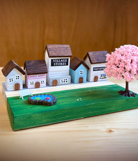 Wooden craft kits for kids - completed model village with miniature houses and a pink tree on a wooden base.